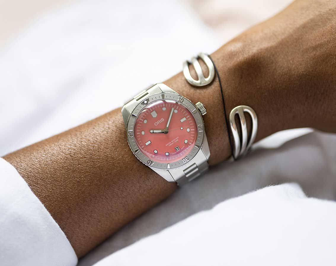 Oris Divers Sixty-Five Cotton Candy Unisex 01 733 7771 4058-07 8 19 18 horloge 38mm met roze wijzerplaat, gedragen aan damespols. Luxe Swiss Made dameshorloge in roestvrijstalen uitvoering.